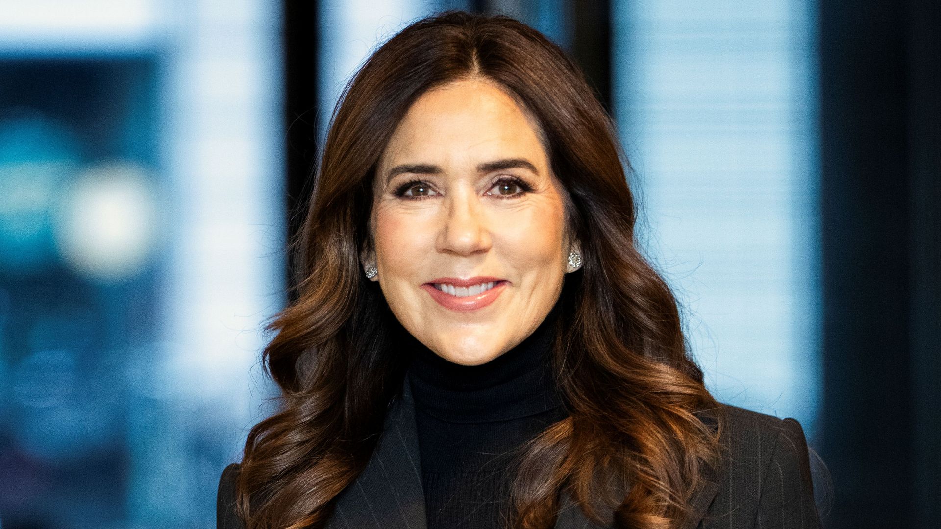 Queen Mary in black suit and rollneck jumper smiling