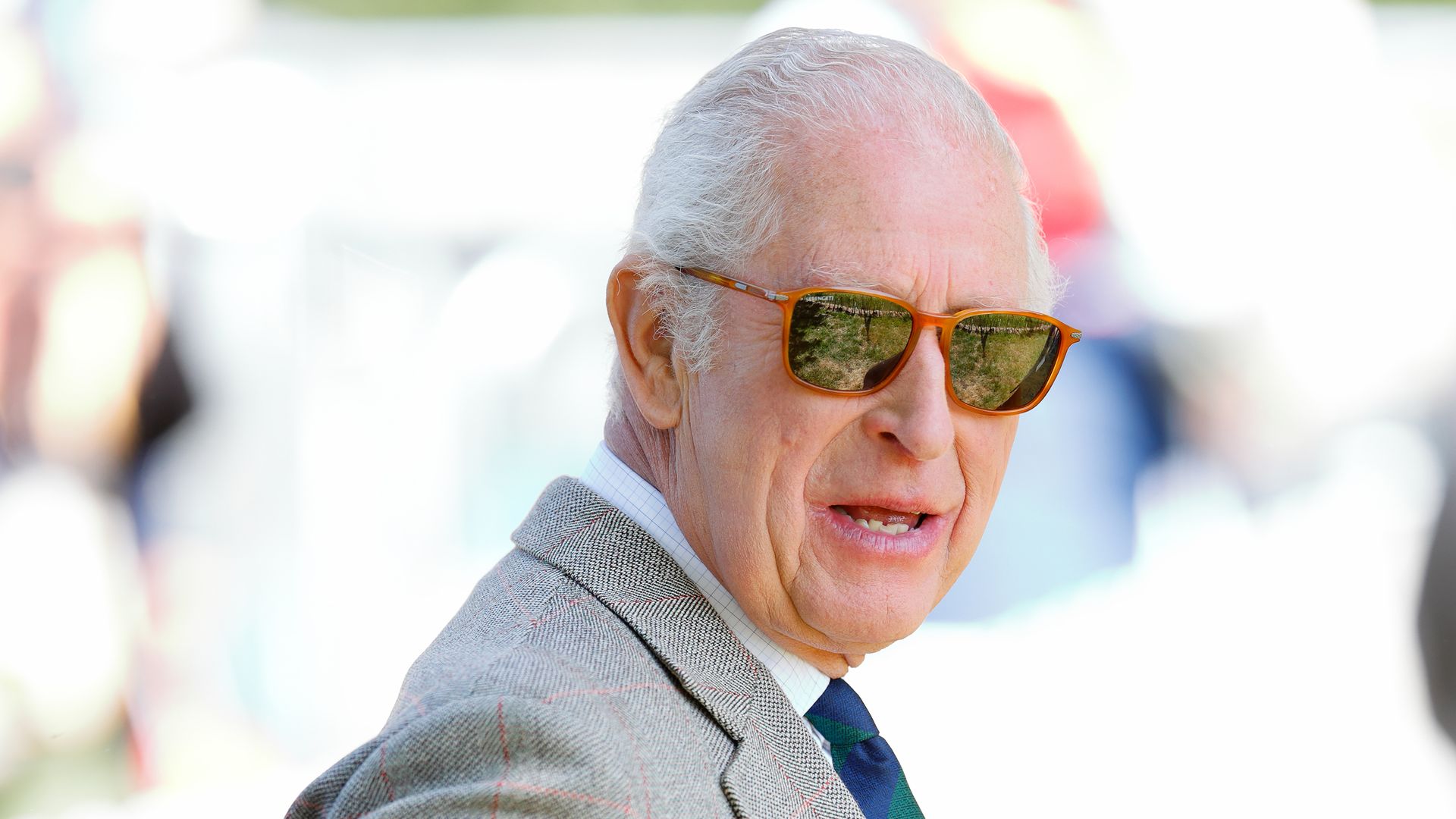 King Charles III wearing suit and sunglasses outside as he walks through grounds of windsor horse show