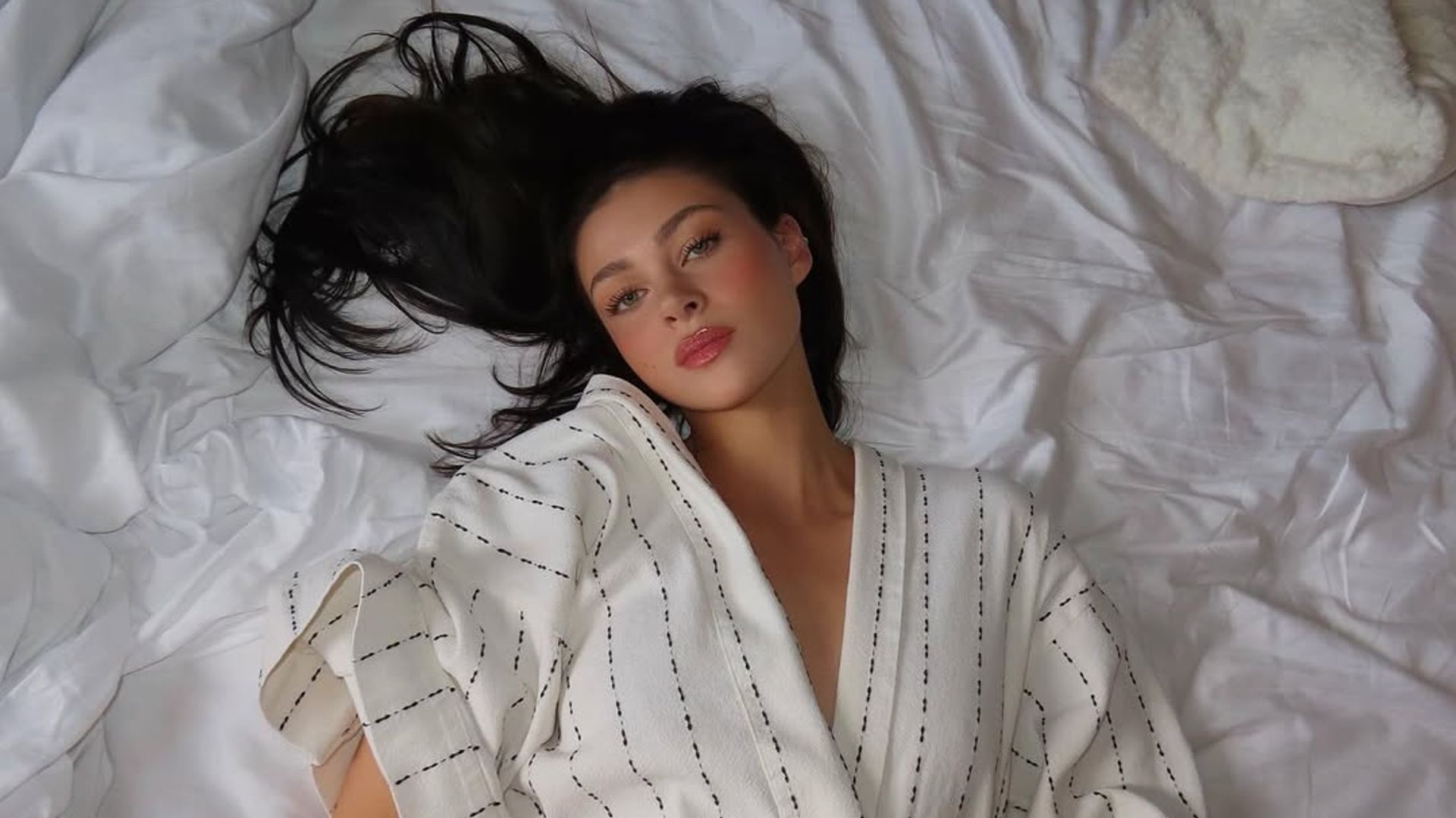 nicola peltz in dressing robe lying on the bed