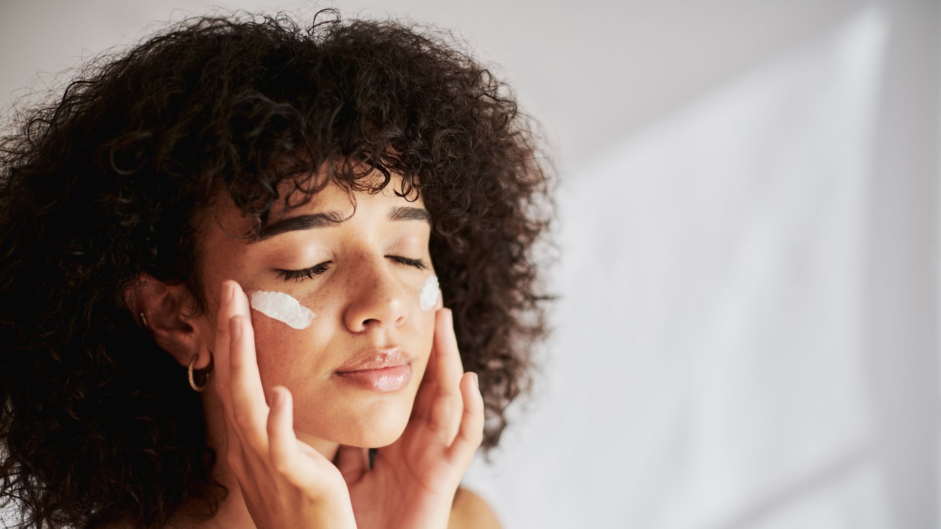 Gen Z model washing face with cleanser in front of white background