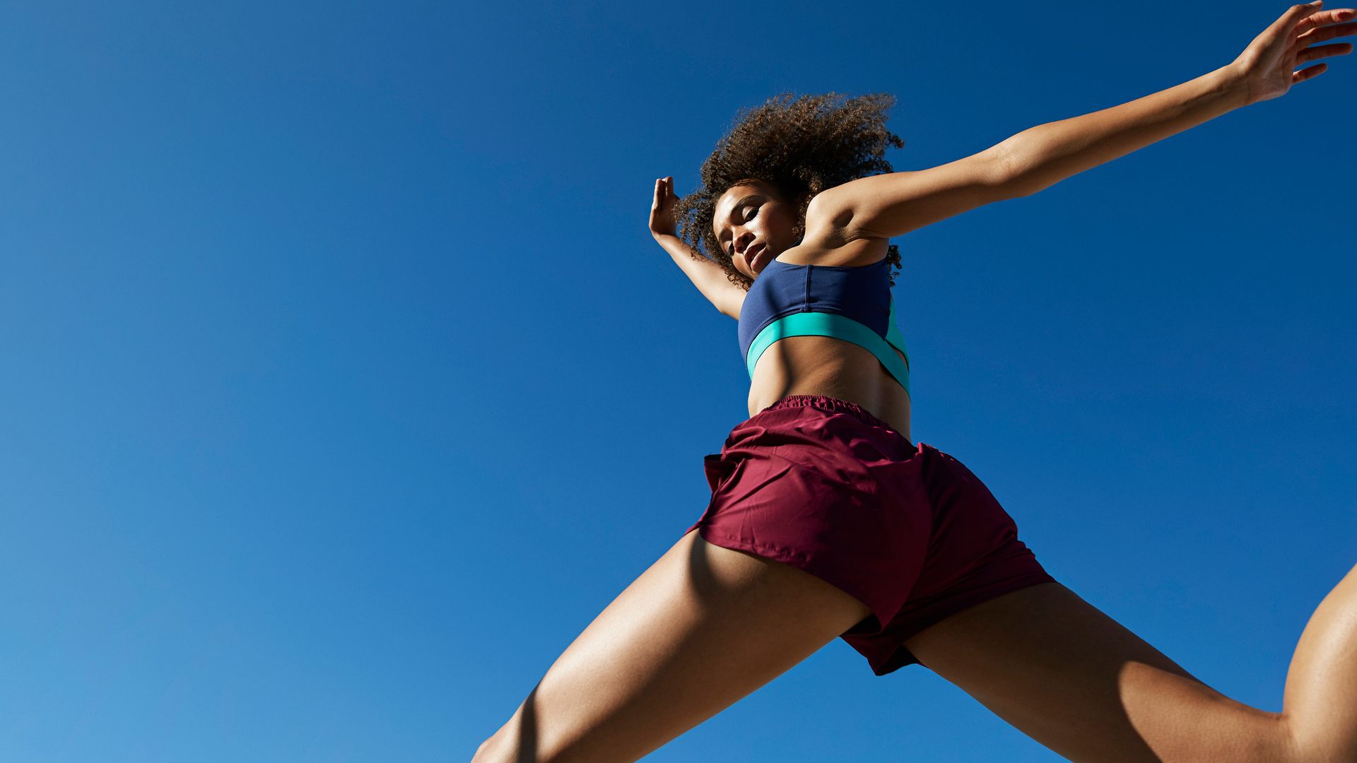 woman jumping against clear blue sky on sunny day