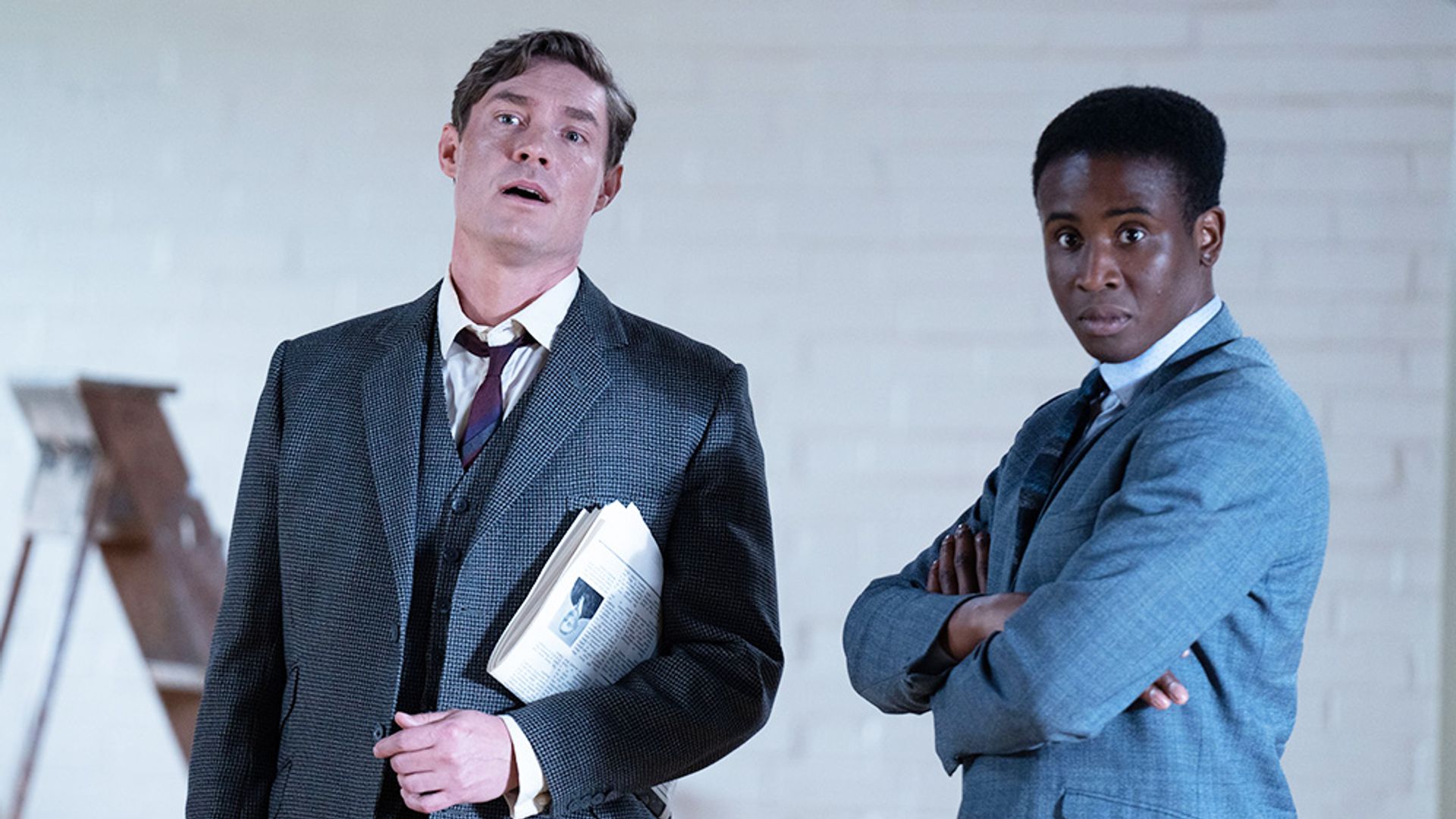 two men in suits standing against white wall