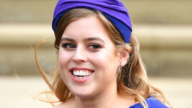 Princess Beatrice smiling in a blue hat at Princess Eugenie's wedding