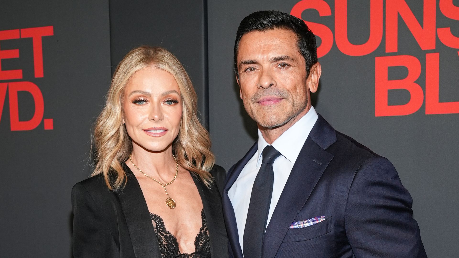 Kelly Ripa in black blazer and lace dress and Mark Consuelos in navy suit 