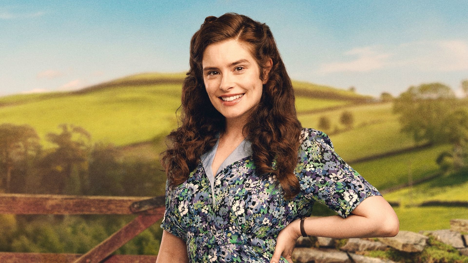 A woman stands in front of a stone wall