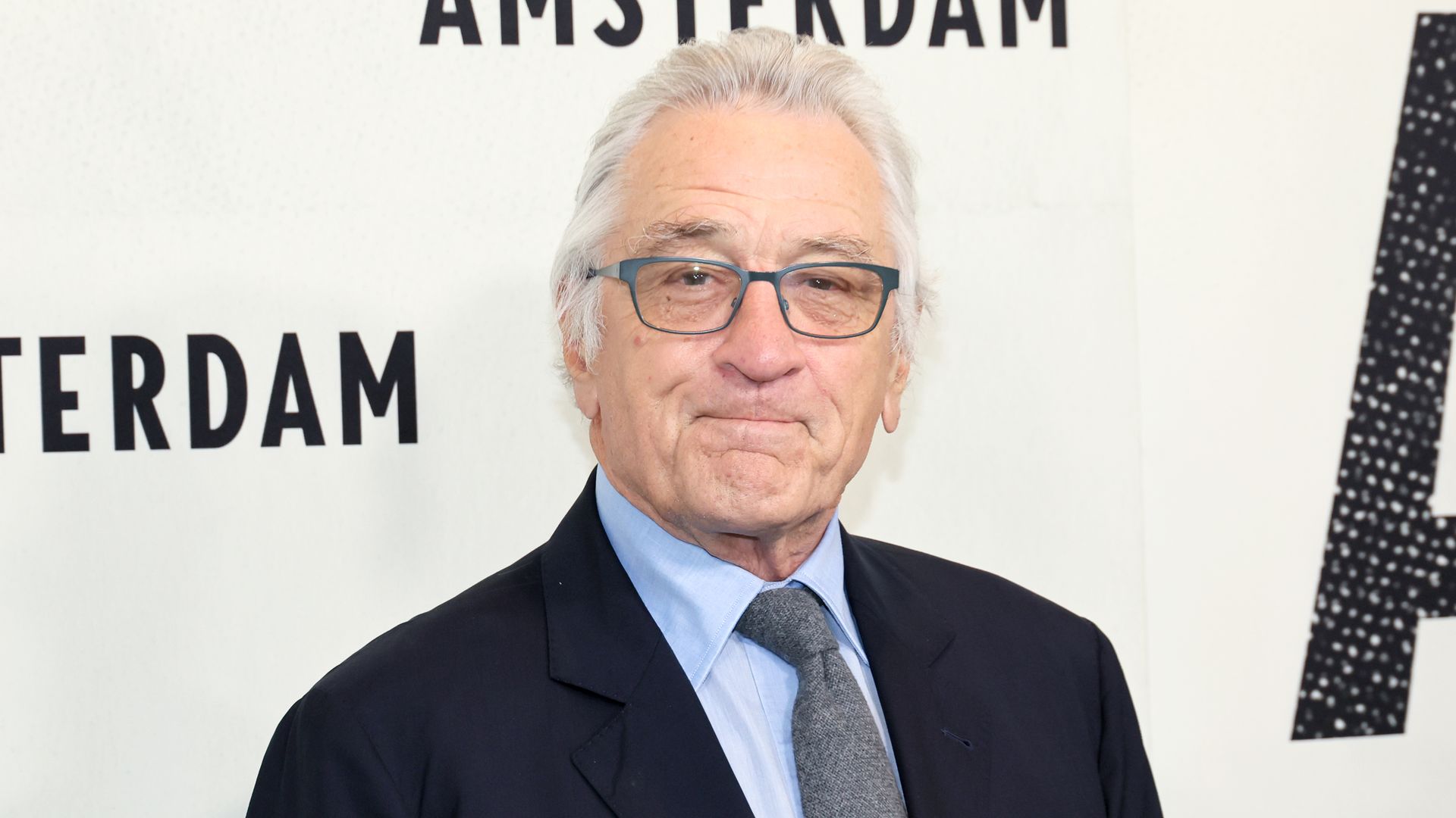 Robert De Niro in a suit and tie standing in white board at film premiere looking at photographers