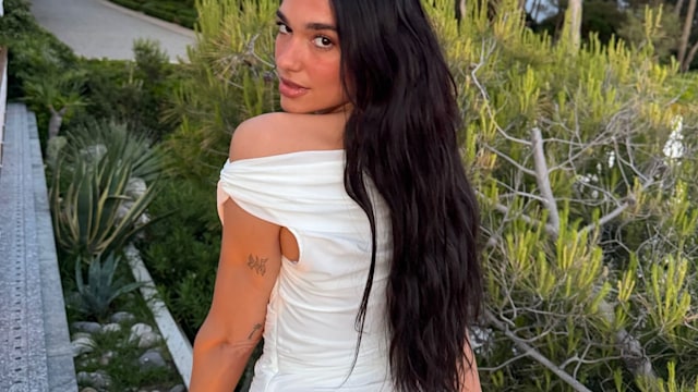 Dua Lipa poses for a photo in a white dress while on holiday with her family