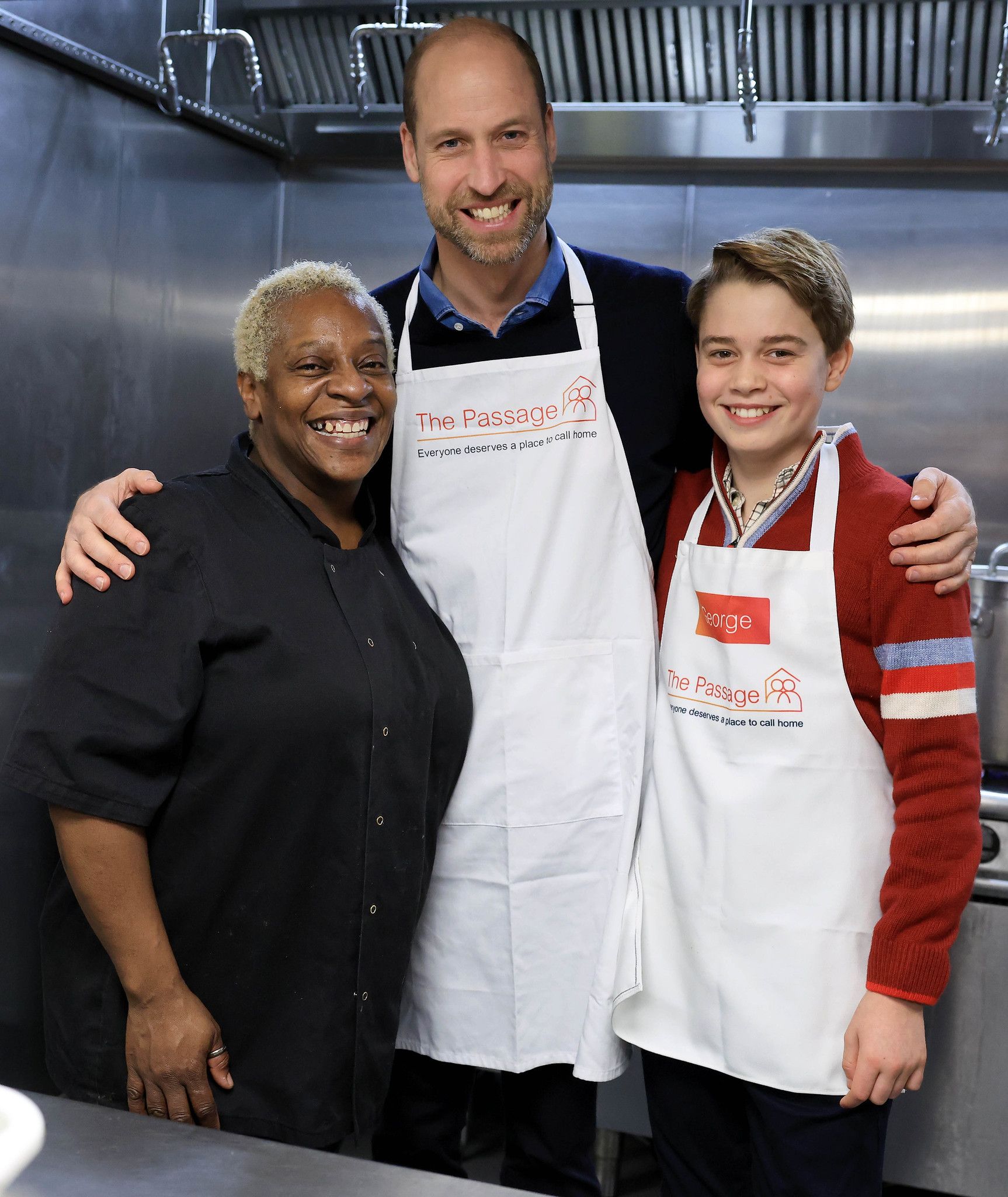 Prince William and Prince George embracing a woman in a grey kitchen