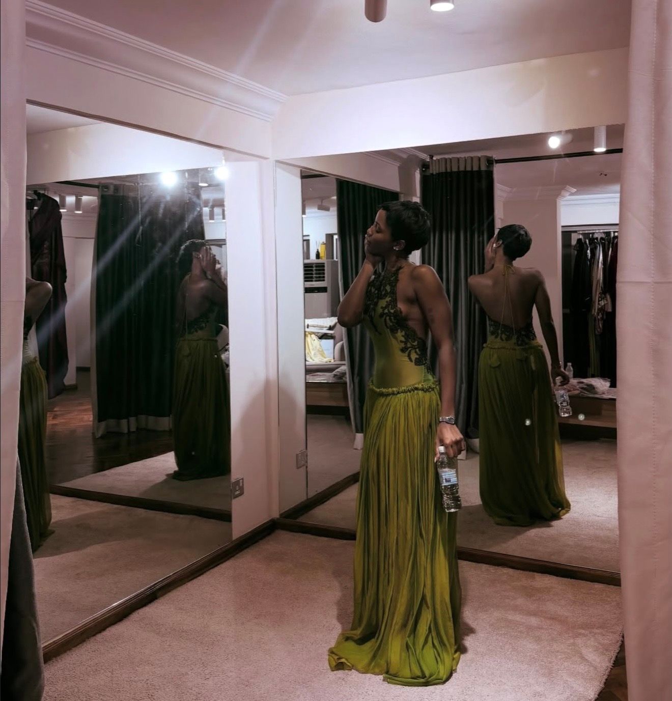 Eva Apio wears a long green dress and poses in a changing room