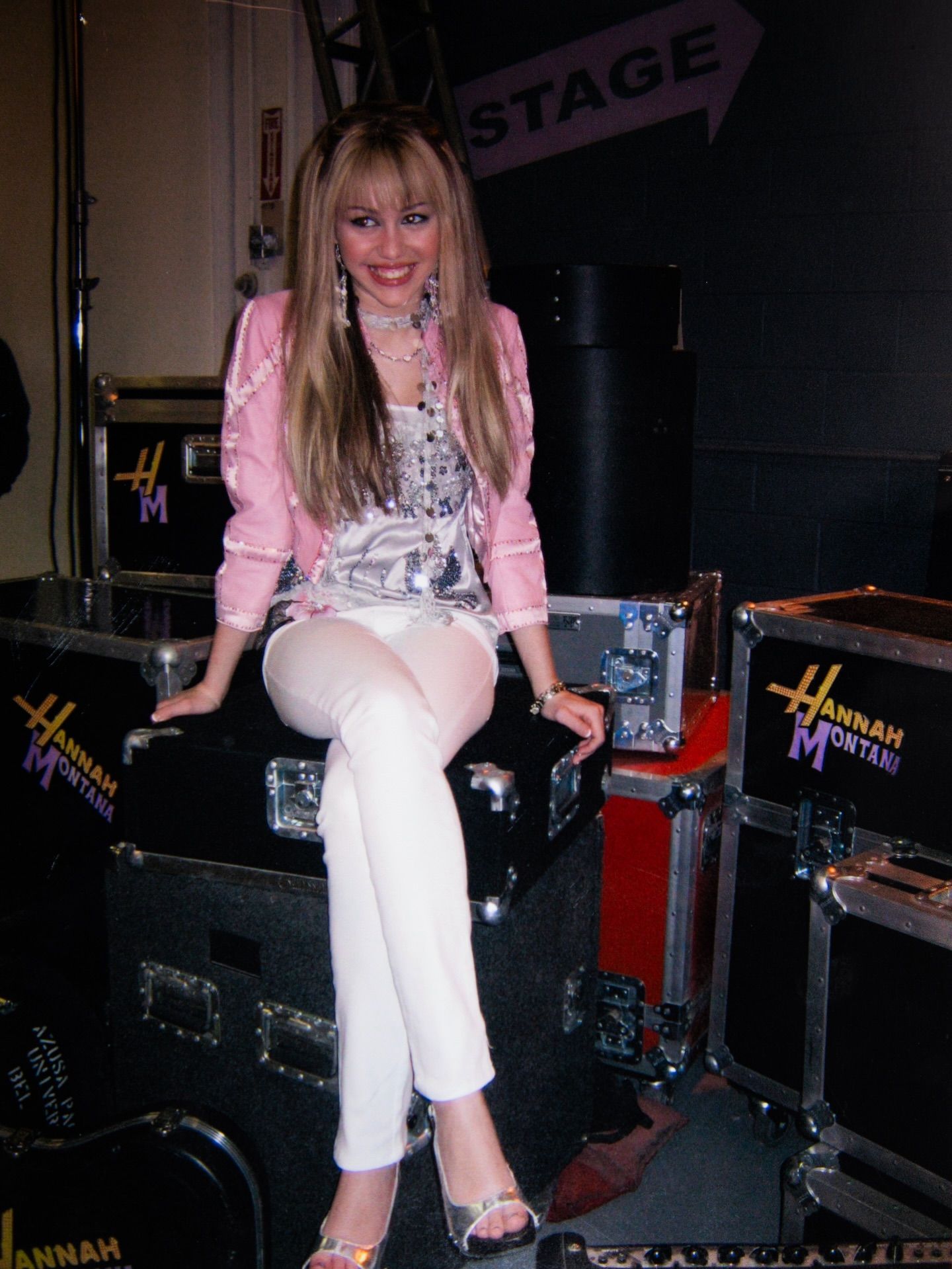 Miley Cyrus habillée en Hannah Montana assise sur un ampli 