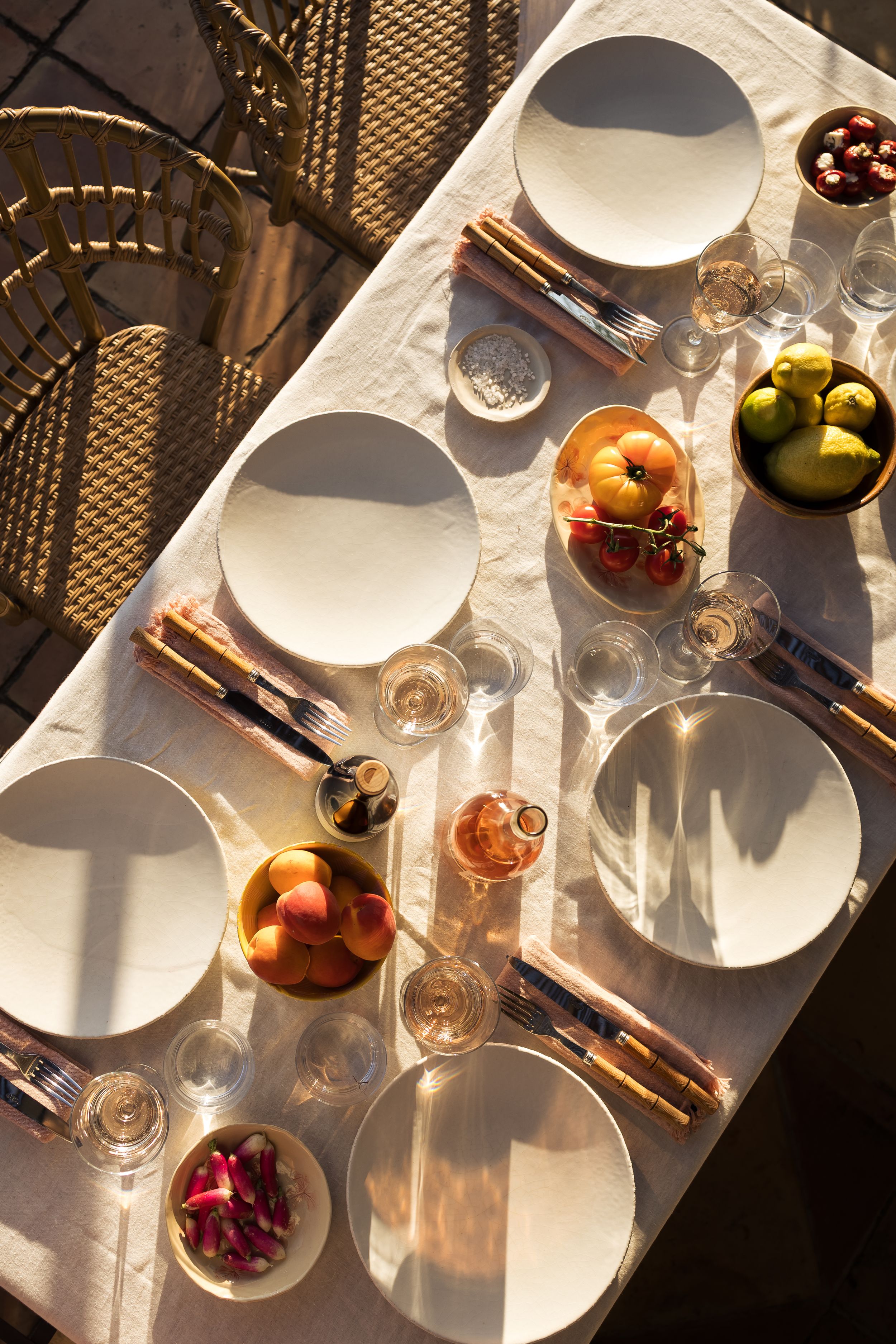 A table laid out in the sunshine with bowls of fruit and glasses of rosé wine in the garden of Domaine Mirabeau