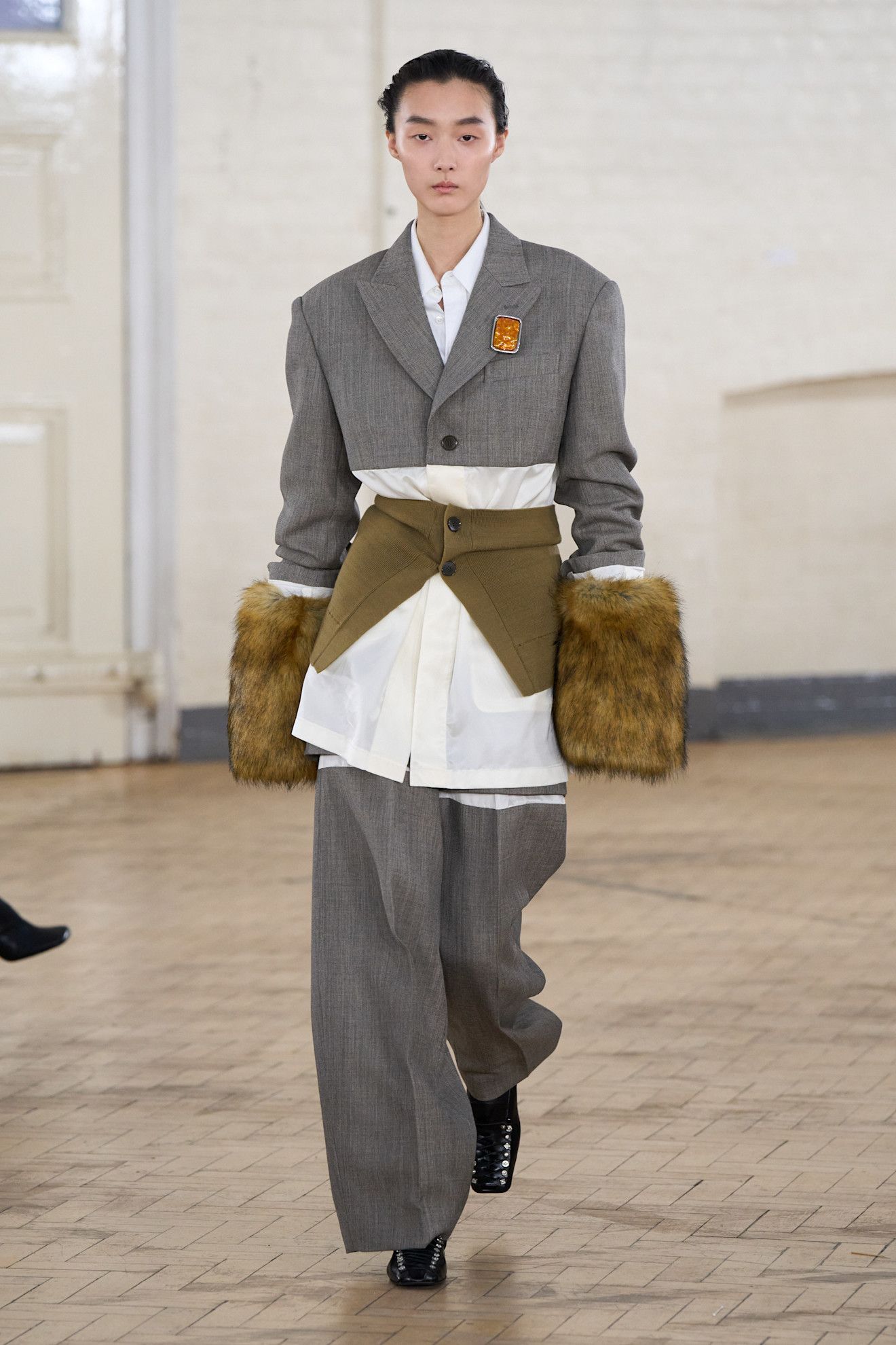 Du drame vintage au nouveau minimalisme, les plus grandes tendances de LFW AW26 14 Un mannequin défile sur le podium vêtu d'un blazer court gris et d'un pantalon assorti avec d'énormes poignets moelleux.