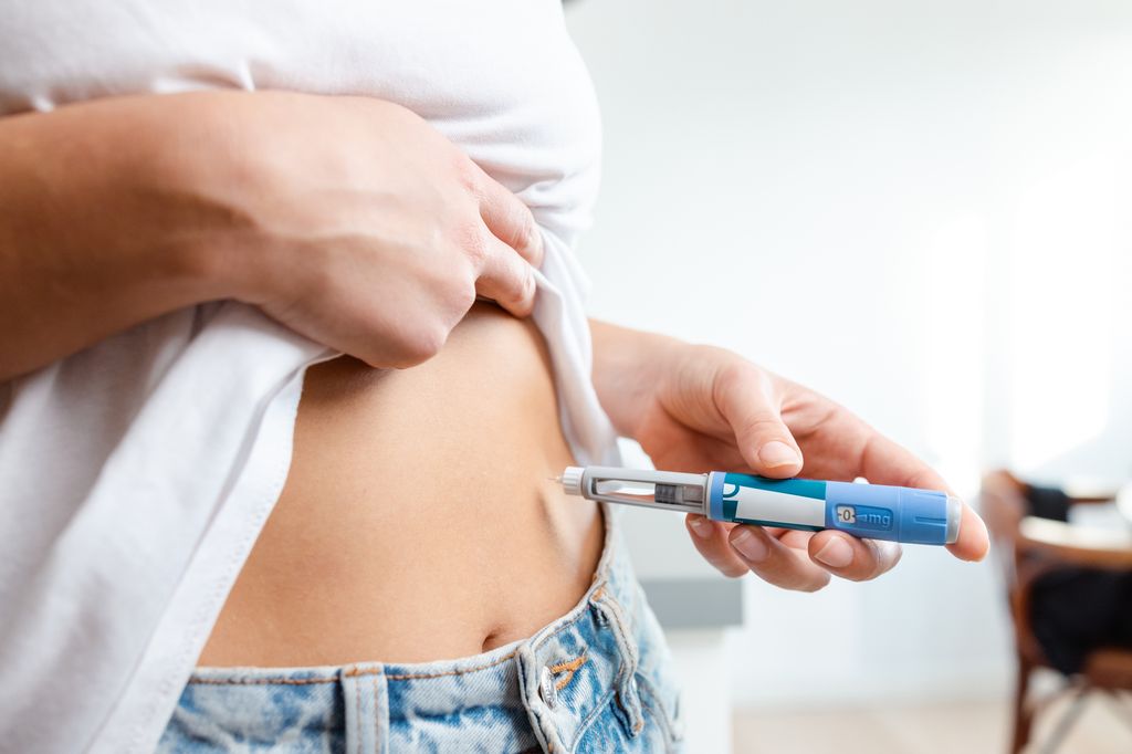 Image of an individual injecting insulin into their abdomen using a pen device. Demonstrates healthcare, diabetes management, and medication administration domestically, conveying a sense of responsibility and self-care.