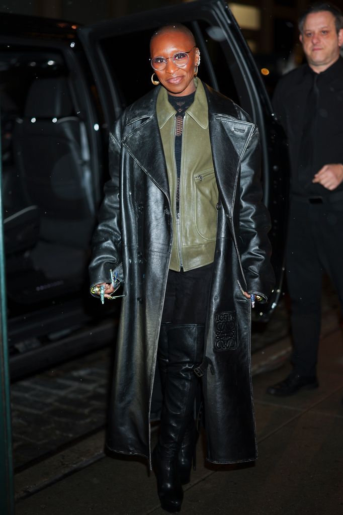 Cynthia Erivo wears a full length black trench coat, black trousers, an olive green leather biker jacket, a black polo neck and thigh high black leather boots in New York. She teamed her outfit with gold jewellery, round glasses and her trademark super long bejewelled manicure