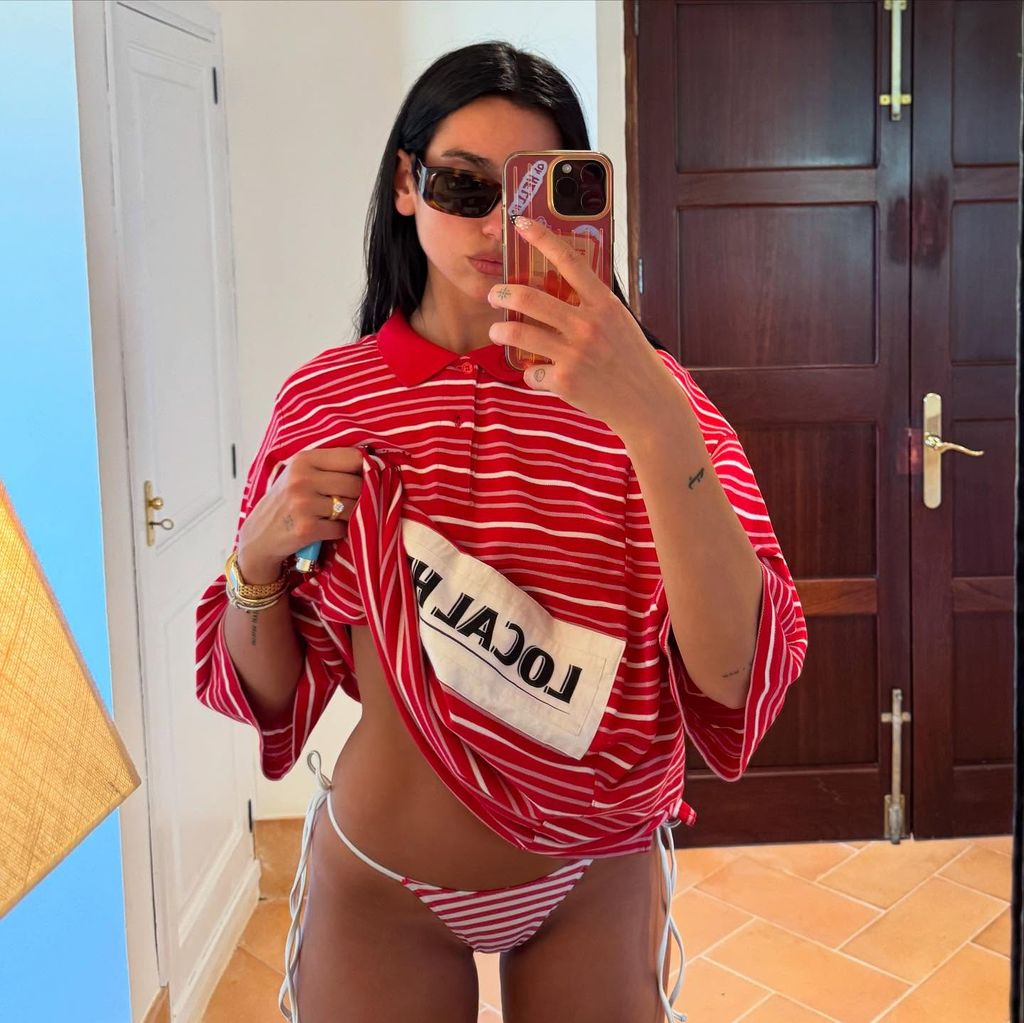 Dua Lipa poses for a mirror selfie in a stripe shirt and matching bikini bottoms