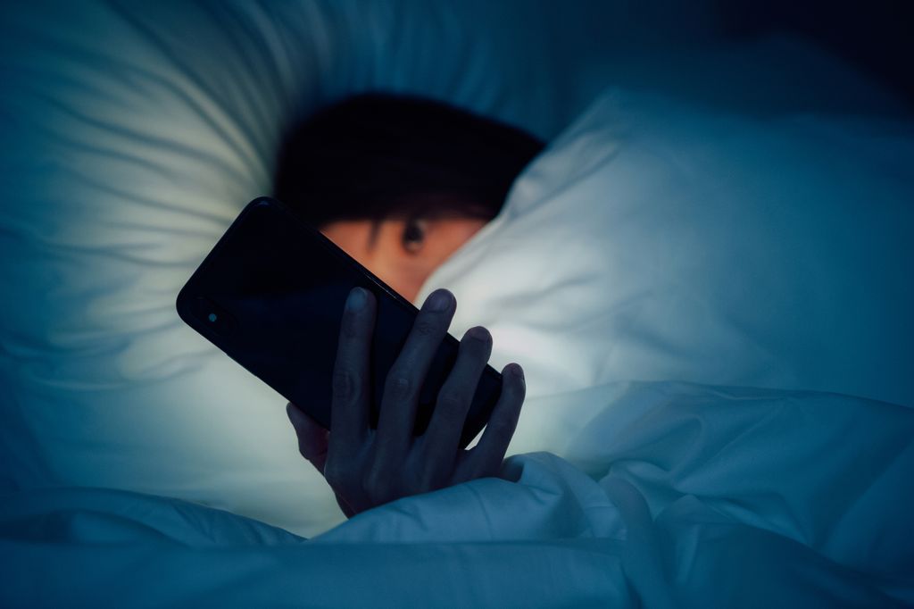 Woman hiding under the blanket, chatting and surfing the internet with smart smartphone at late night on bed. Working late concept 