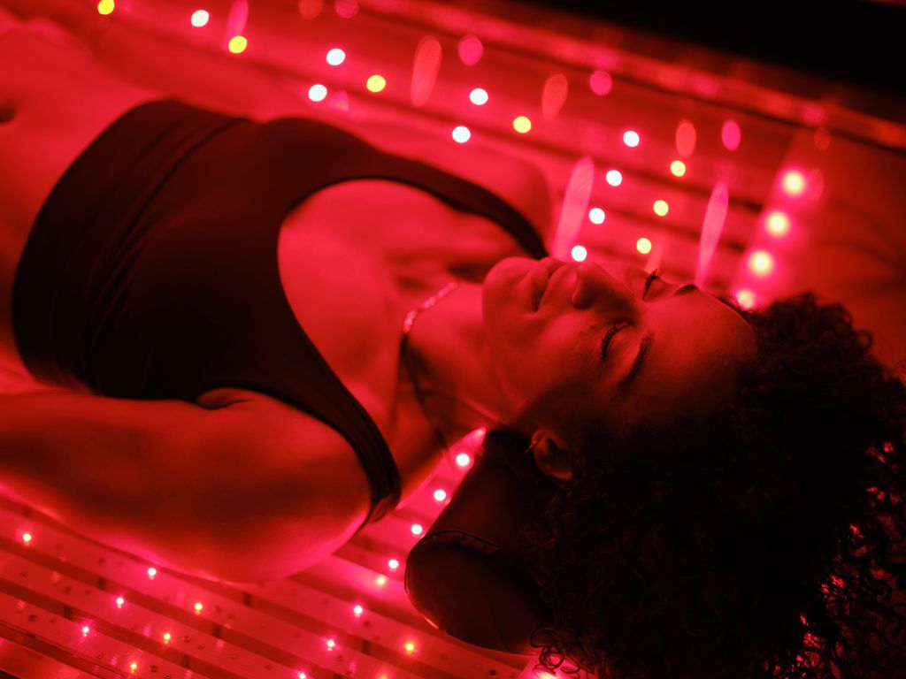 A multiracial woman on an LED light bed, receiving red light therapy.