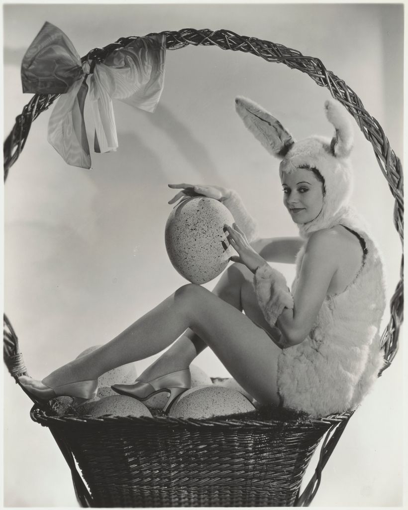 Heather Angel dressed in a furry bunny suit and ears sits in a giant Easter basket holding an egg.