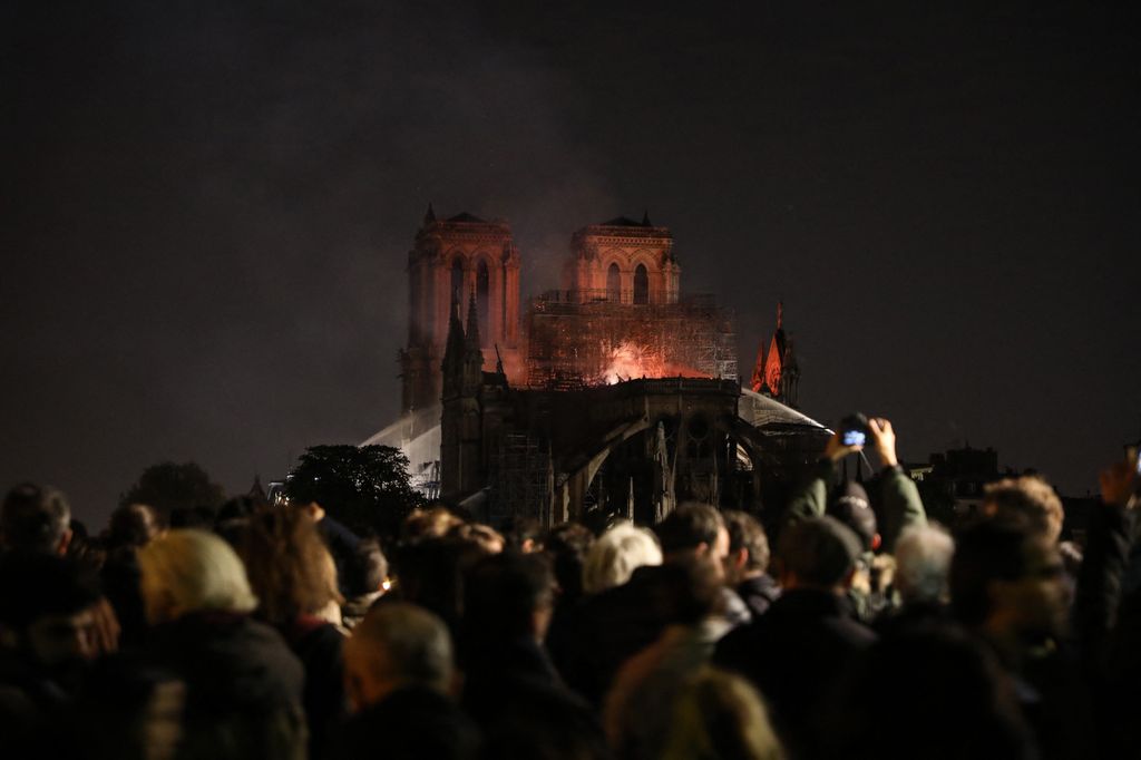 People watch as Notre-Dame de Paris Cathedral burns late into the night on April 15, 2019, in the French capital Paris. A huge fire swept through the roof of the famed Notre-Dame Cathedral in central Paris on April 15, 2019, sending flames and huge clouds of grey smoke billowing into the sky. The flames and smoke plumed from the spire and roof of the gothic cathedral, visited by millions of people a year.