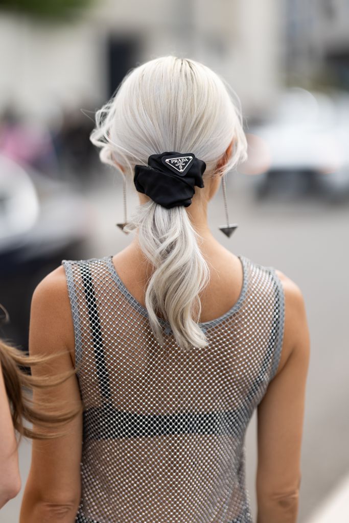 A guest wears Prada pendant earrings, a Prada black hairband, a black bra and a rhinestones fishnet silver tank top outside Prada show during the Milan Fashion Week Menswear Spring/Summer 2025 on September 19, 2024 in Milan, Italy.