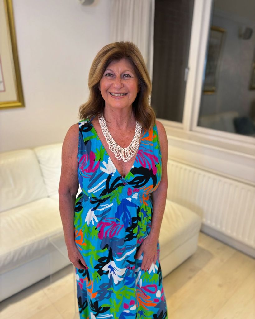 Tina Pemberton standing in her living room smiling wearing a bright blue floral dress