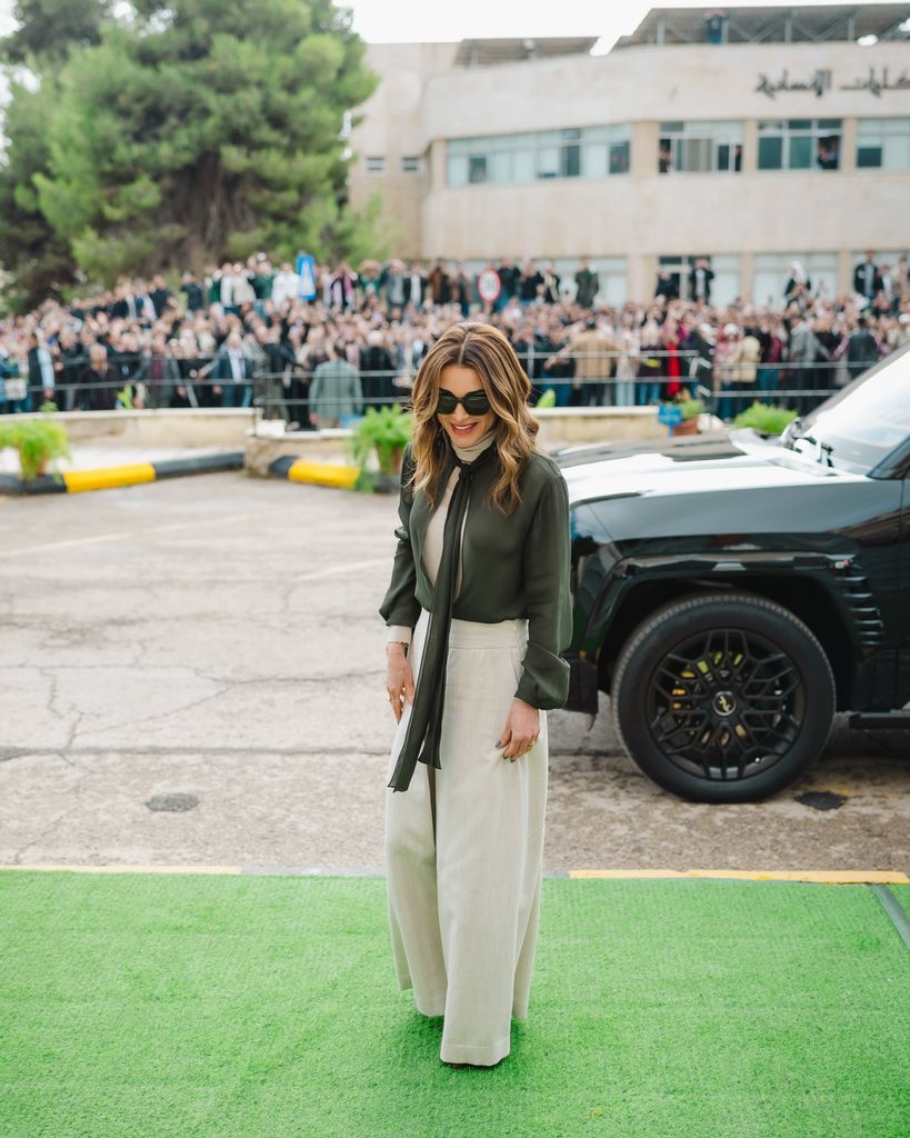 Rania outside venue in cream trousers and khaki blouse