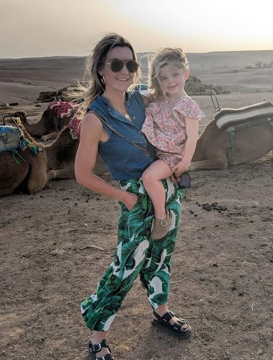 Helen Skelton holding her daughter Elsie with three camels behind them