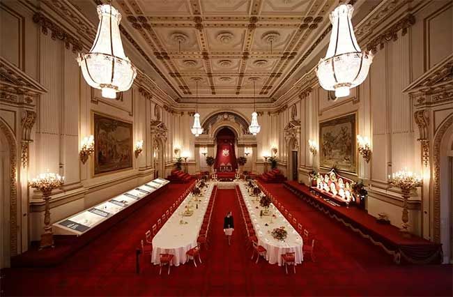 a huge red carpeted state room with large crystal chandeliers and two long white clothed tables