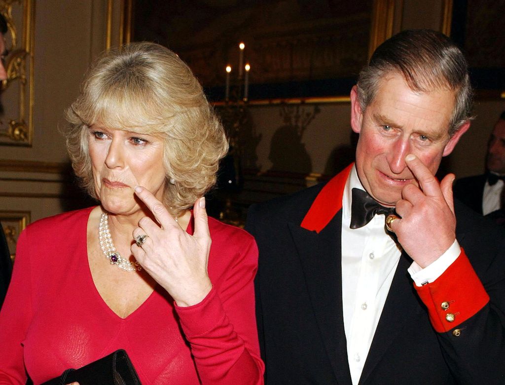 King Charles and Queen Camilla holding their fingers to their faces