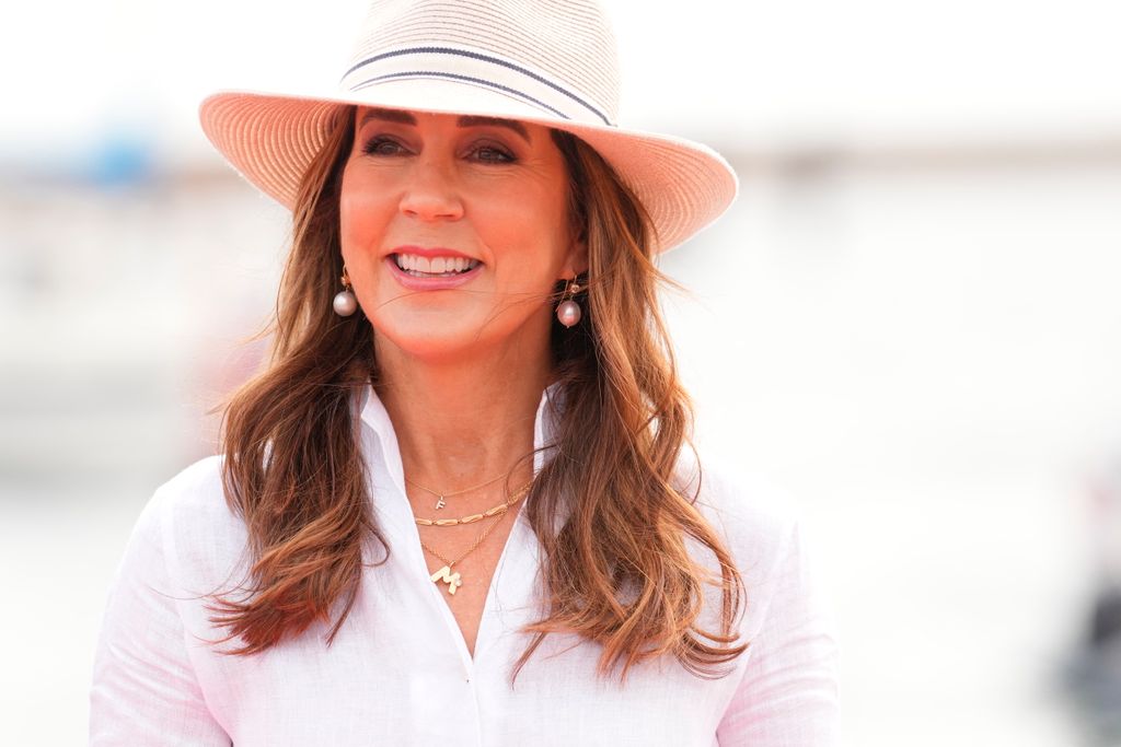 Queen Mary wearing hat, white shirt and gold necklaces