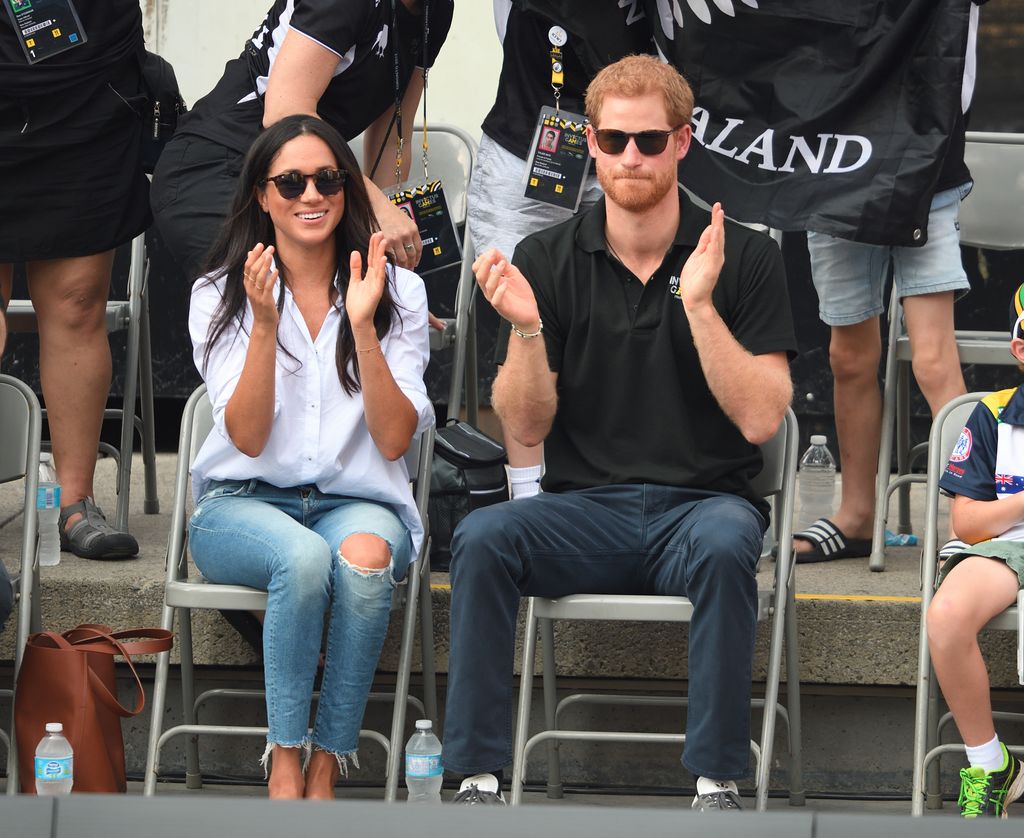 Meghan in super casual ripped jeans sitting with prince harry