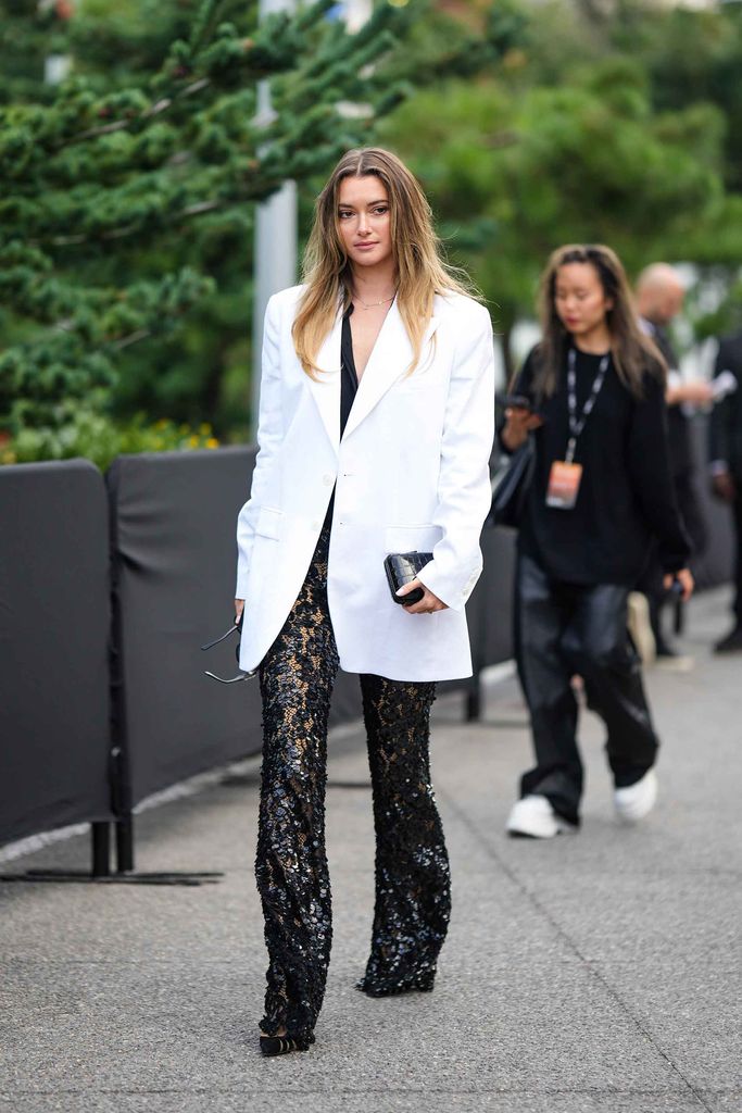 A guest wears a white oversized blazer jacket, mesh sequined flared pants, outside Michael Kors, during New York Fashion Week