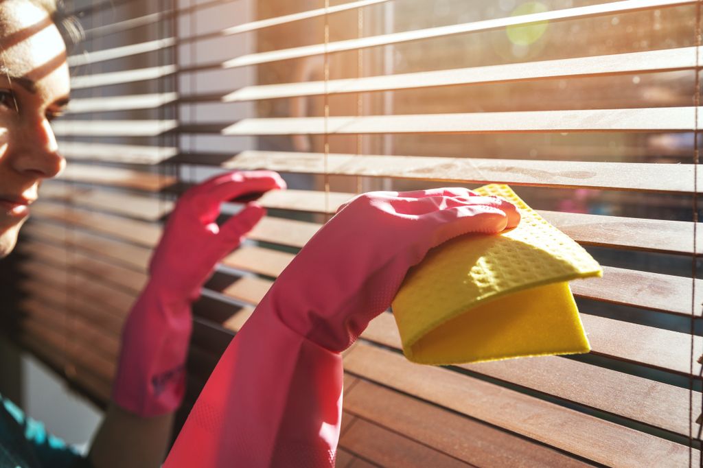 A woman cleaning blinds in her home