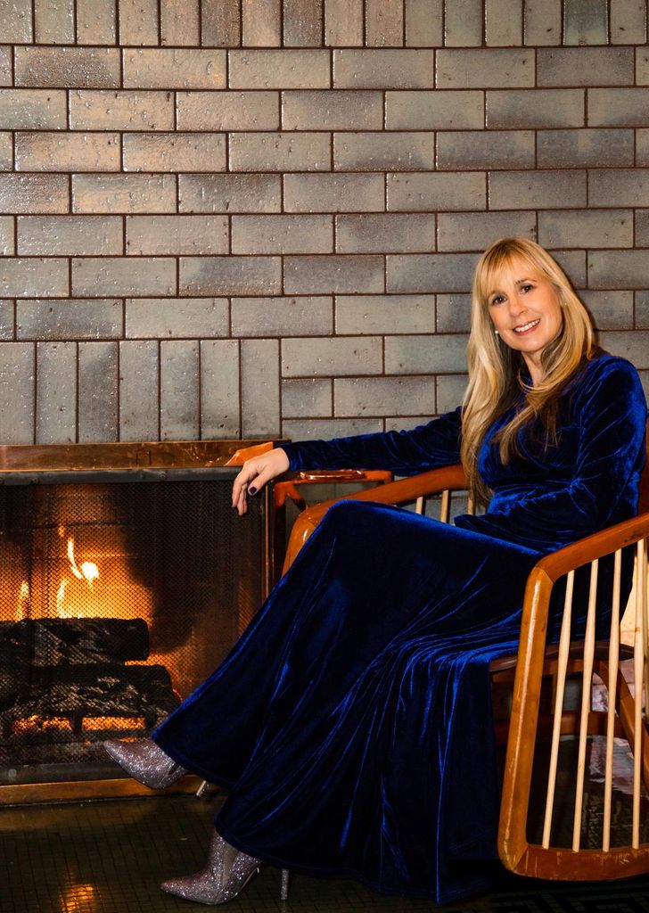 Theresa sat in a chair in front of a fire 