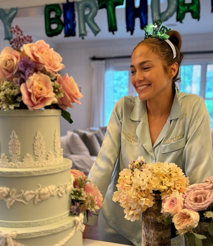 Jennifer Lopez stands in front of a three-tier birthday cake