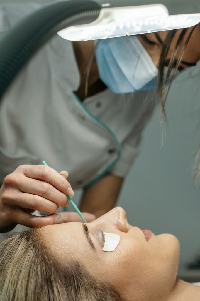 Young woman with beautiful clean skin having a lash lift treatment. She is laying on the bed, her eyes are closed and the beautician is doing the treatment.