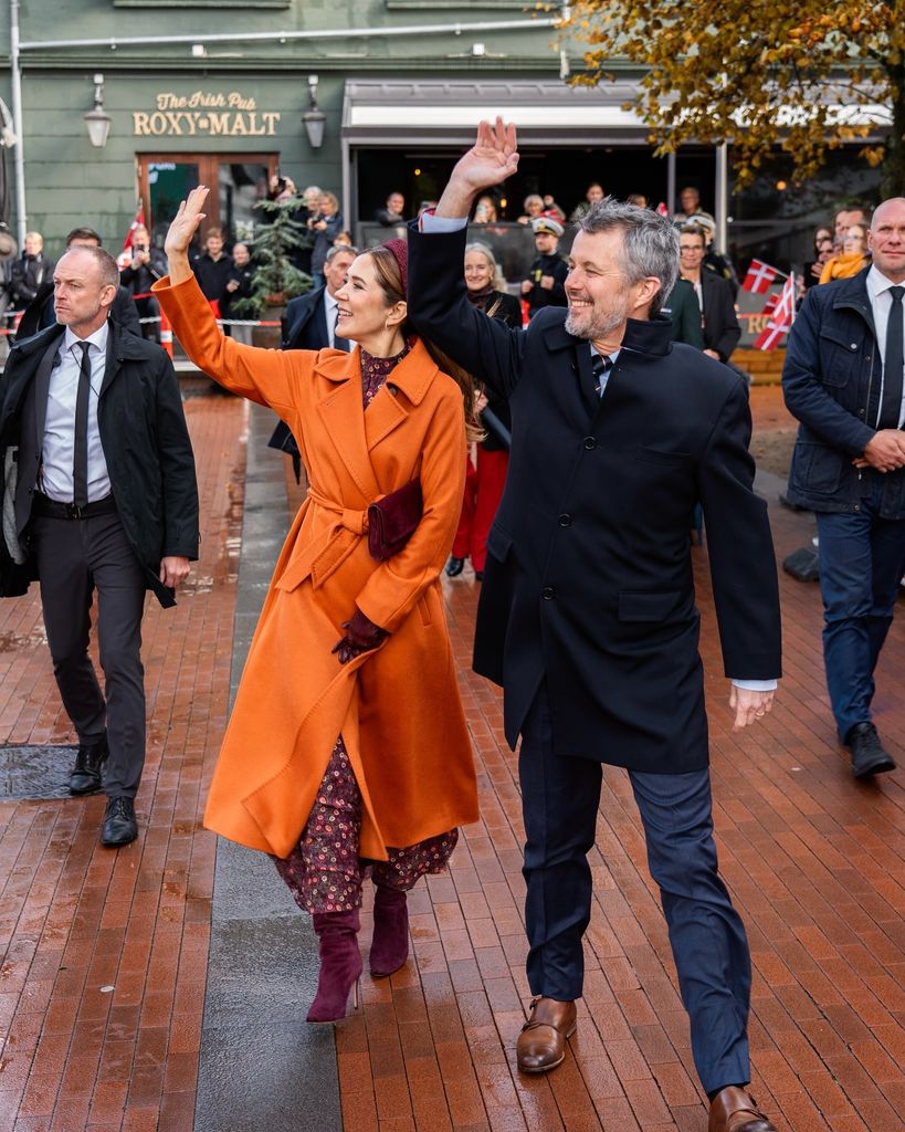 Queen Mary waving in burnt orange coat beside Frederik