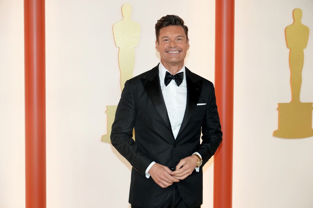 Ryan Seacrest in a suit smiling on the Oscars red carpet