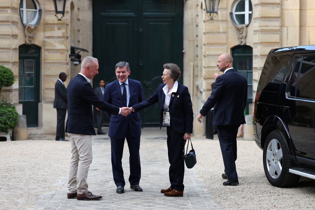 Princess Anne in a smart suit shaking hands with a man in a blazer