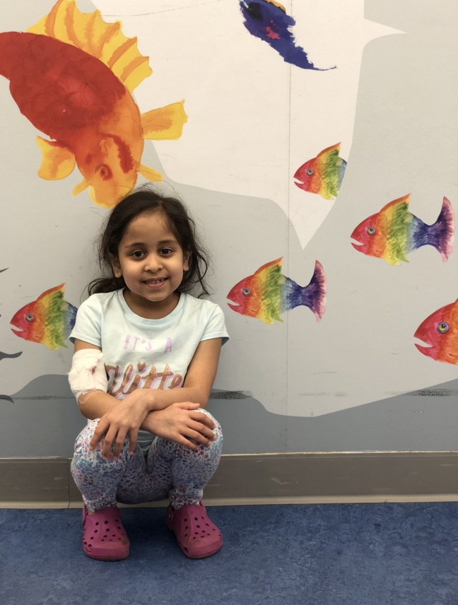 little girl crouching against wall covered in fish