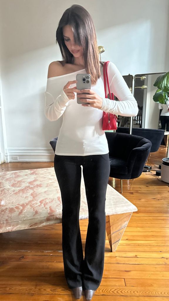 Emily Ratajkowski poses for a mirror selfie in a white long sleeve and black trousers