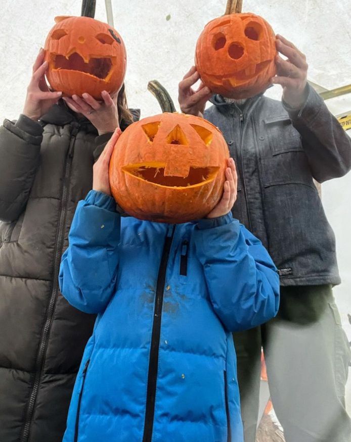 Three people hiding their faces with pumpkins