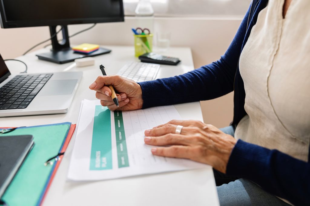 Close-up view of middle aged businesswoman reviewing data analysis documents while working at home office