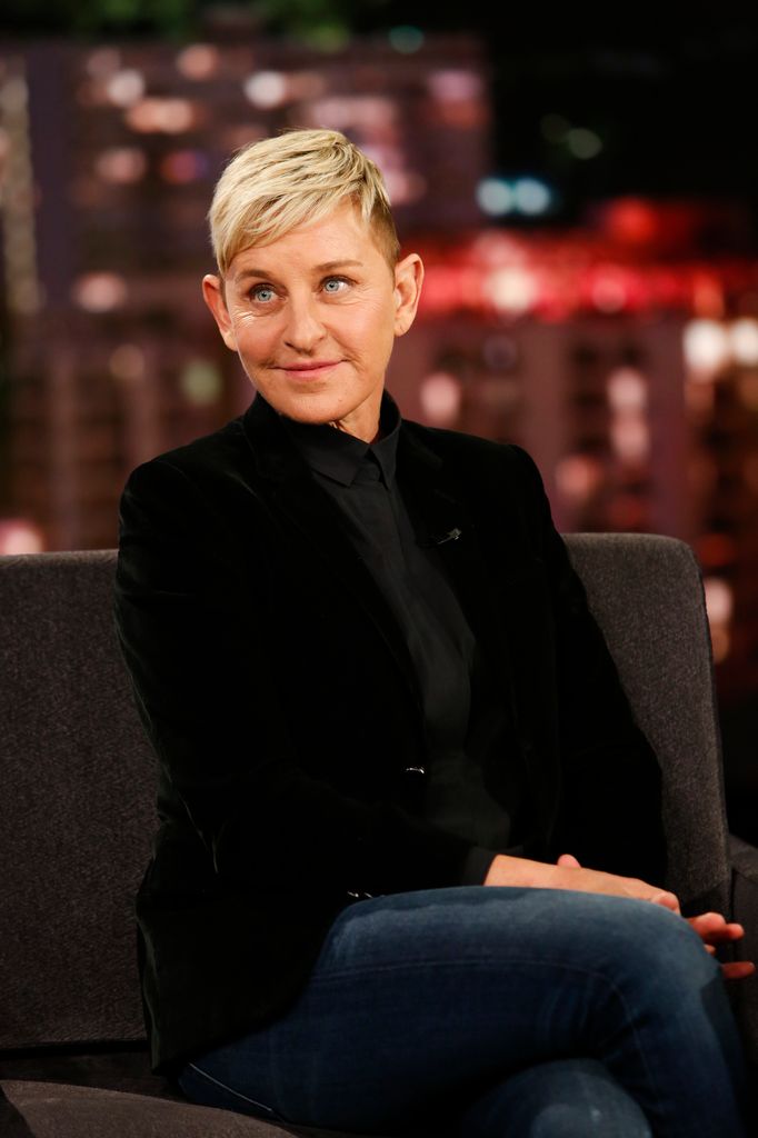 Ellen DeGeneres wearing dark suit sitting on a sofa and smiling at the camera during TV appearance