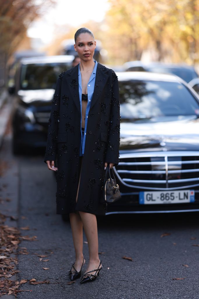 Nara Smith est vue portant une tenue complète de Miu Miu, composée d'un blazer noir à la longueur du genou avec des revers et des épaulettes en notation avec un embellissement à paillettes noir floral, une chemise bleue midle en dessous, un soutien-gorge noir orné de paillettes noires