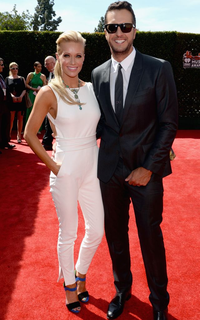 Caroline Boyer in a white jumpsuit in the red carpet with suit-clad Luke Bryan
