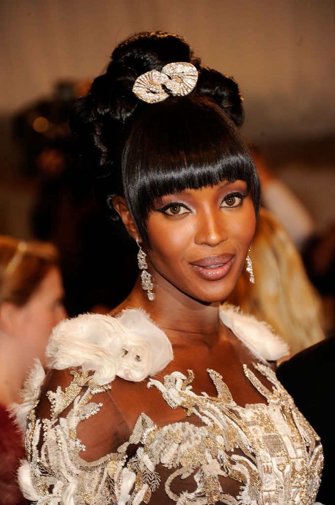 Naomi Campbell at the 2011 Met Gala wearing fan-shaped clips in her hair and chandelier earrings with an embellished feathered gown.