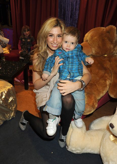 stacey kneels down with a toddler on her knee dressed in a blue check top as they smile at the camera while surrounded by ginormous stuffed teddy bears