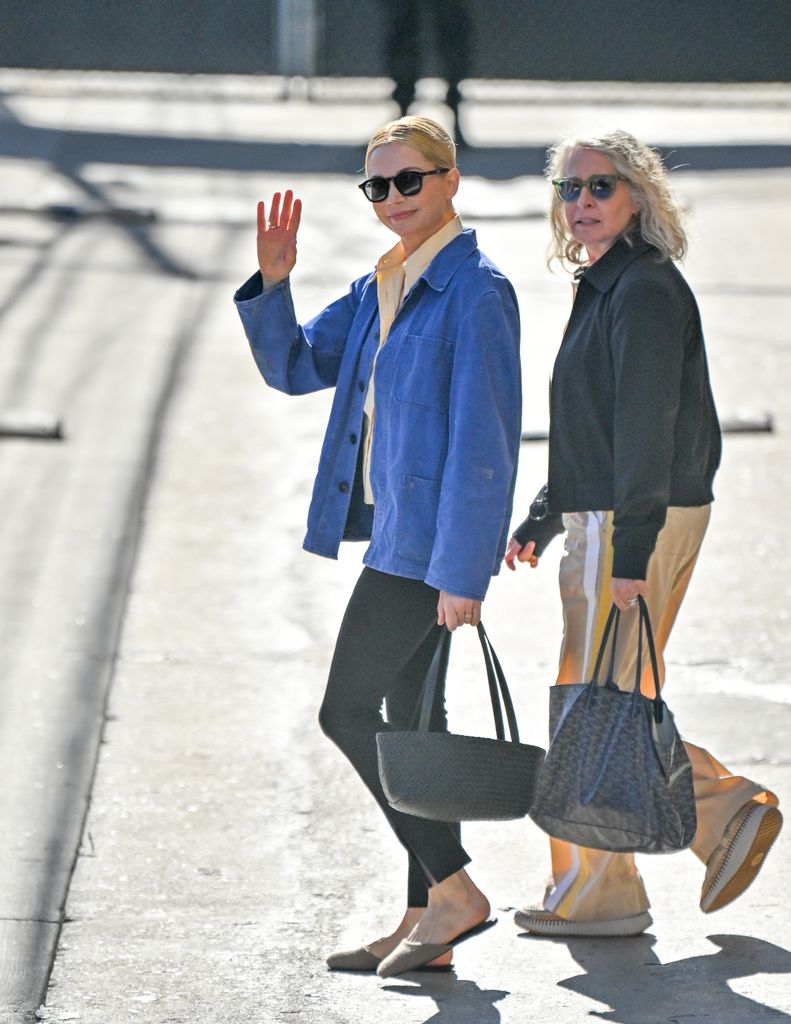 Michelle Williams waving to camera in jeans and blue jacket