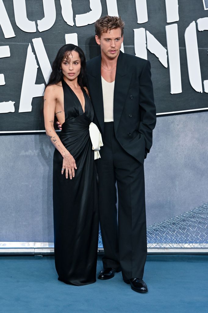 Zoë Kravitz and Austin Butler stand on the red carpet, both wearing black. Austin's arm is around Zoë's waist